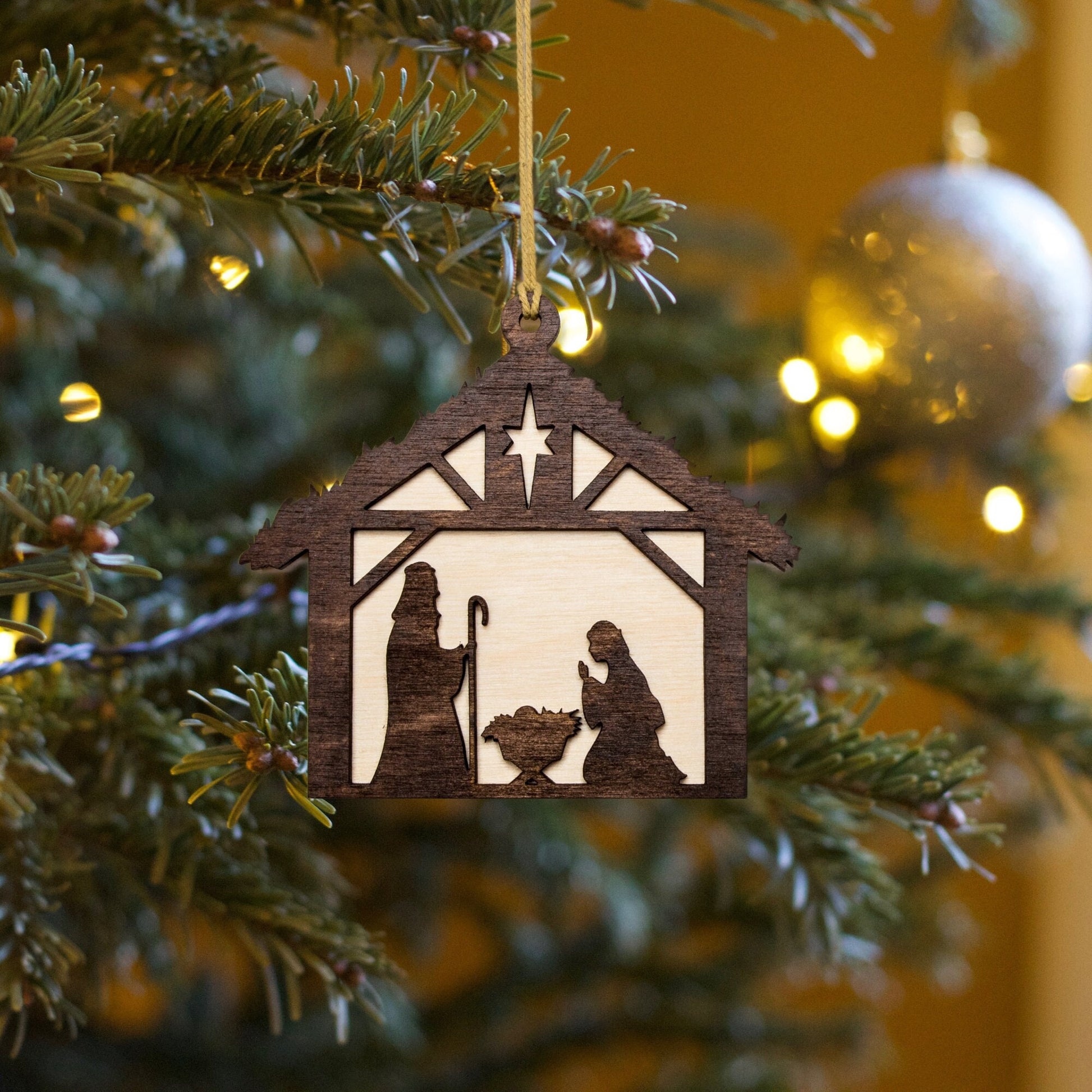 a christmas ornament hanging from a christmas tree depicting a nativity scene